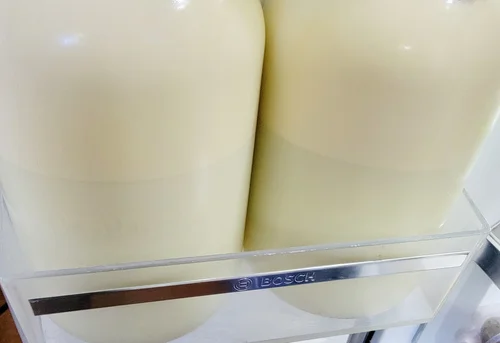 Two large containers of creamy liquid stored in a Bosch refrigerator, showcasing a smooth texture and pale color.